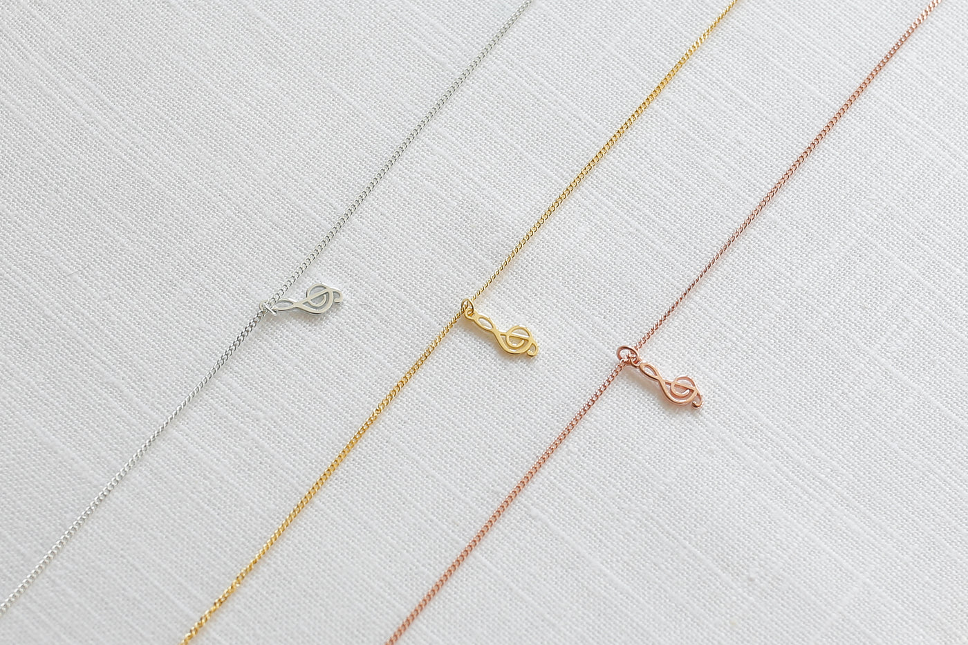  Drei Musikschlüssel Ketten in jeweils Sterlingsilber, Gold und Rosegold auf Leinen 
