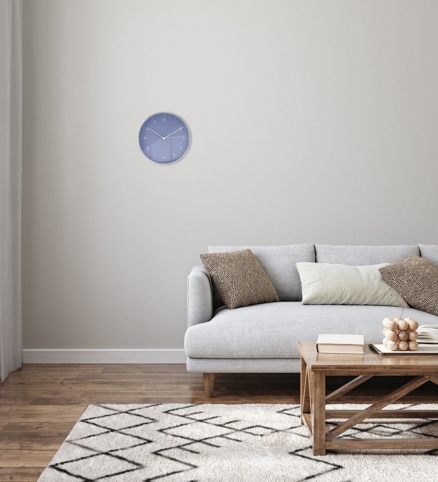 Wanduhr in Hellblau und Silber hängt im Wohnzimmer über grauer Couch