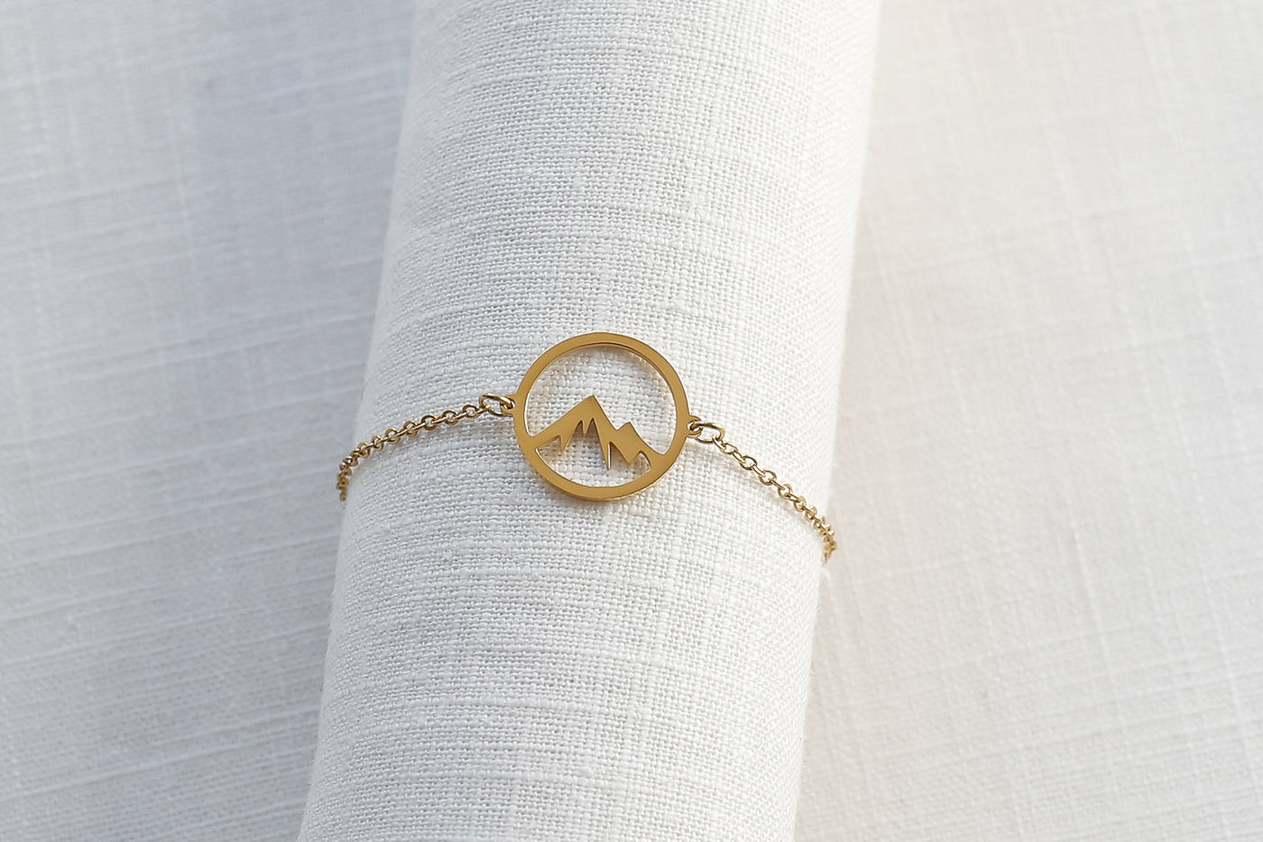 Armband mit Bergspitze Anhänger und verstellbare Länge in Gold platziert auf Leinen Stoff