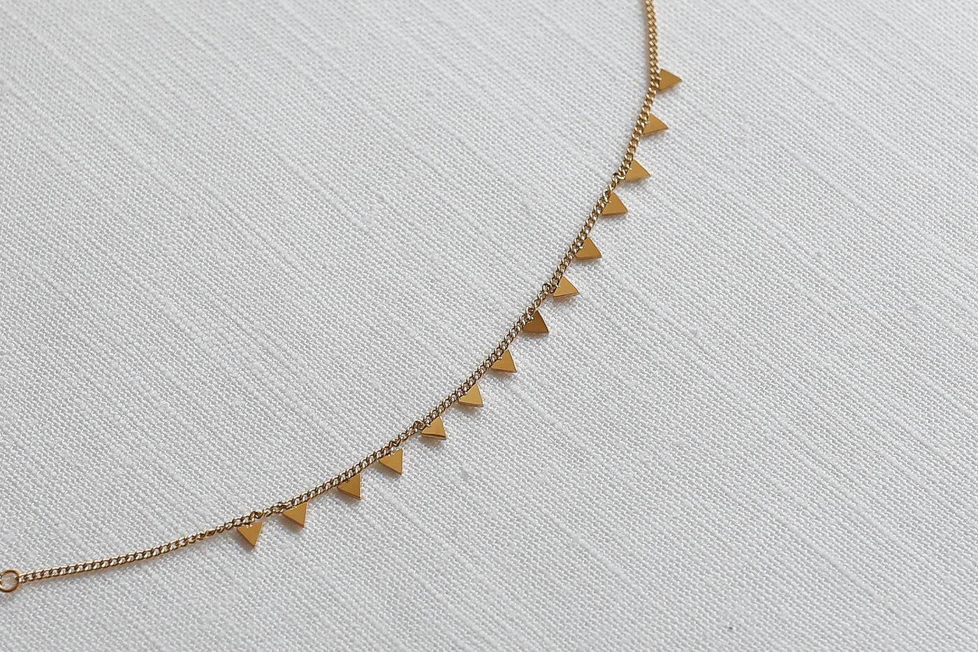 Armband mit Dreieck Plättchen Anhängern und verstellbarer Länge in Gold platziert auf Leinen Stoff.