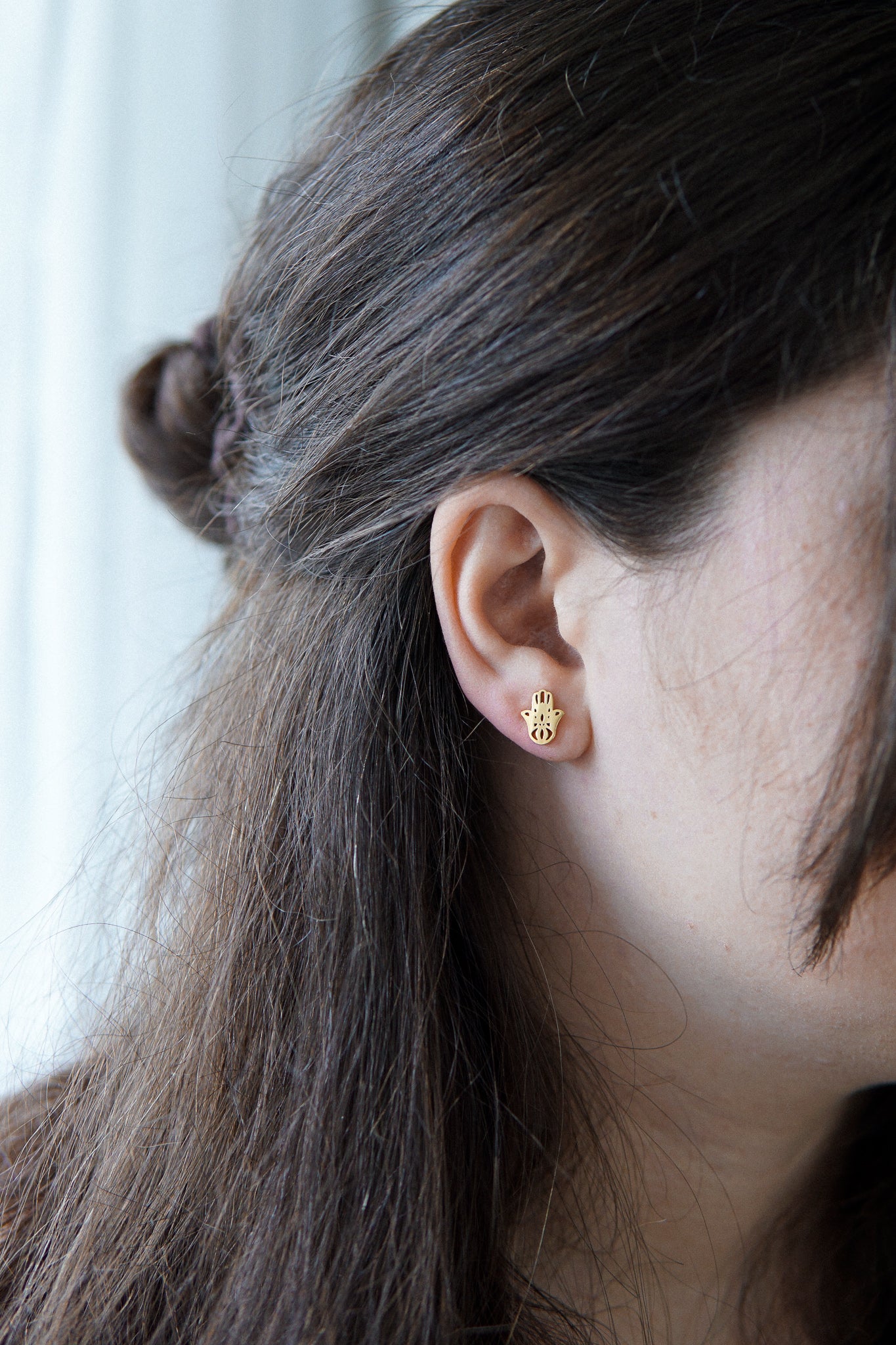 Junge Dame trägt vergoldete Ohrstecker mit Hamsa Hand Stecker
