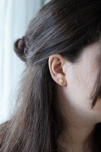 Junge Dame trägt vergoldete Ohrstecker mit Hamsa Hand Stecker