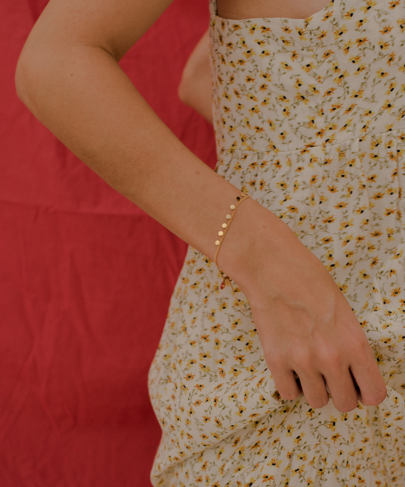 Dame trägt Armband mit Kreis Anhängern in Gold vor rotem Hintergrund