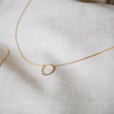  Feminine Halskette mit geometrischem Anhänger in Gold auf einem Stoff Tuch 