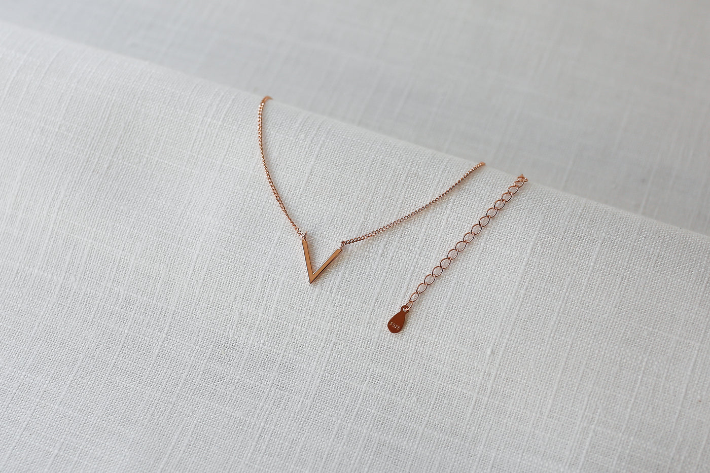 Rose farbene Halskette mit V Anhänger im Boho Stil auf Leinen Stoff