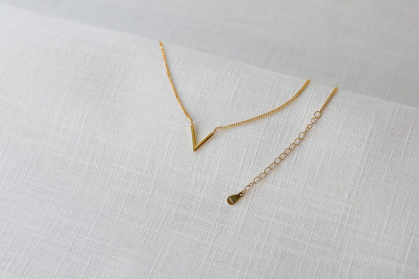 Filigrane Gold Kette mit V Anhänger und verstellbarem Verlängerungsverschluss auf einem Leinen Tuch 