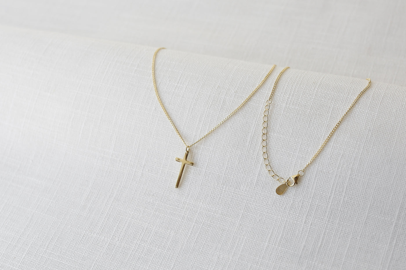 Feminine Halskette mit Kreuz Anhänger in Gold auf einem Stoff Tuch 