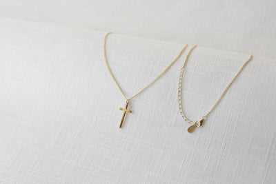 Feminine Halskette mit Kreuz Anhänger in Gold auf einem Stoff Tuch 
