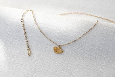 Kette mit Ginkgo Blatt Anhänger und verstellbarer Länge in gold platziert auf Leinen Stoff 