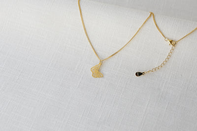 Feminine Halskette mit Schmetterling Anhänger in Gold auf einem Stoff Tuch 