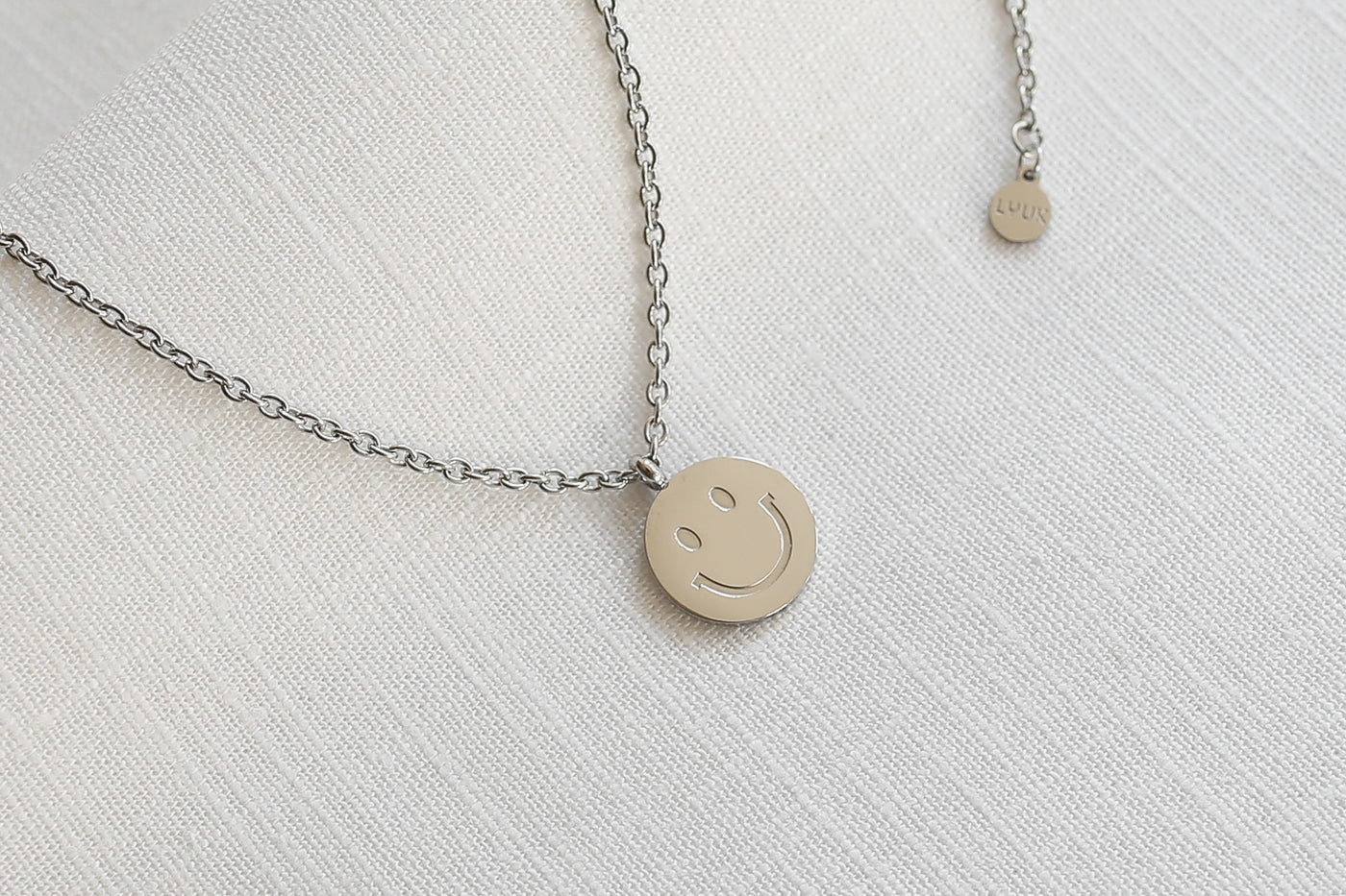 Filigrane Kette mit Smiley Anhänger in Silber auf weißem Leinen Tuch.