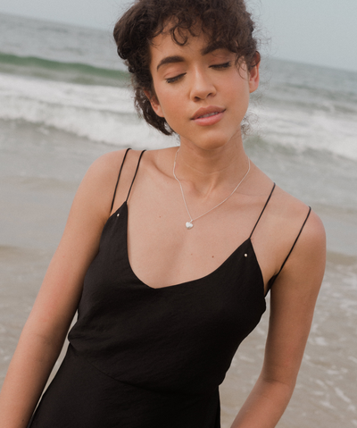 Junge Frau trägt feine silberne Kette mit Herz Anhänger im minimalistischen Stil am Strand 