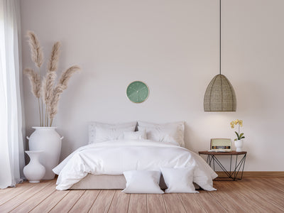 Dunkelgrüne Wanduhr hängt über weißem Bett im Boho Stil 