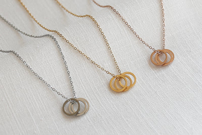 Drei stilvolle Halsketten mit Ring Anhängern in jeweils Silber, Gold und Rosegold auf Stoff