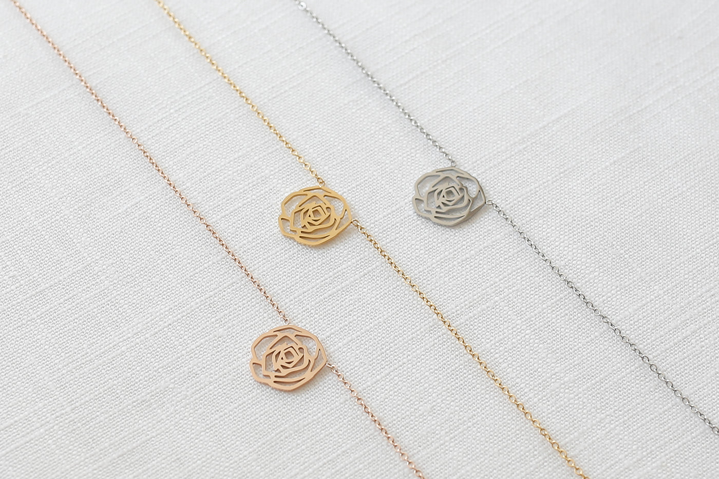 Drei alltagstagstaugliche Halsketten mit Rosenblüten Anhänger in jeweils Silber, Gold und Roségold auf Stoff