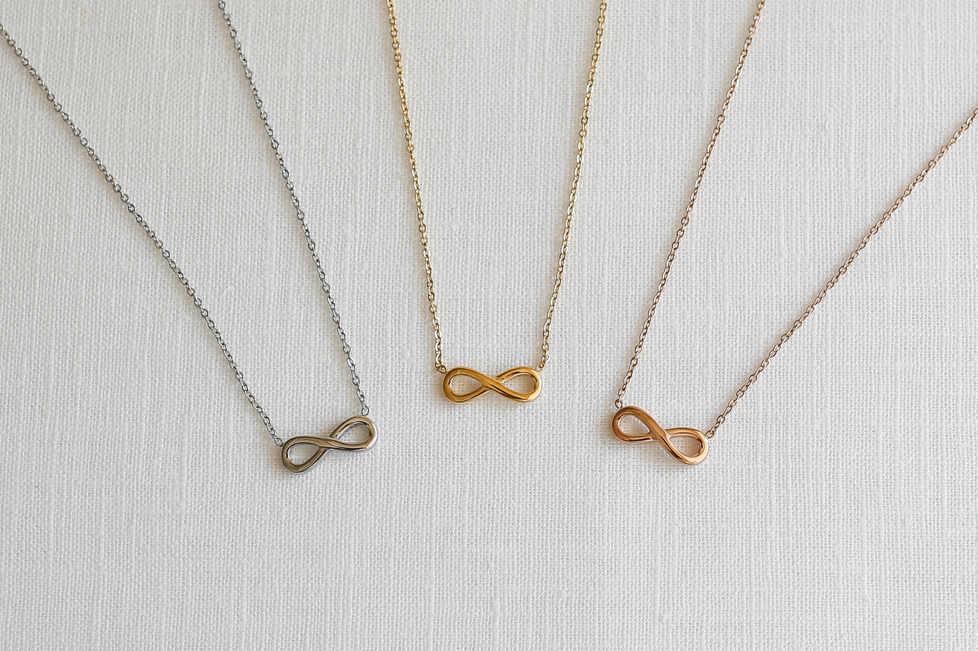  Drei alltagstaugliche Halsketten mit Infinity Anhänger in jeweils Silber, Gold und Roségold auf Stoff