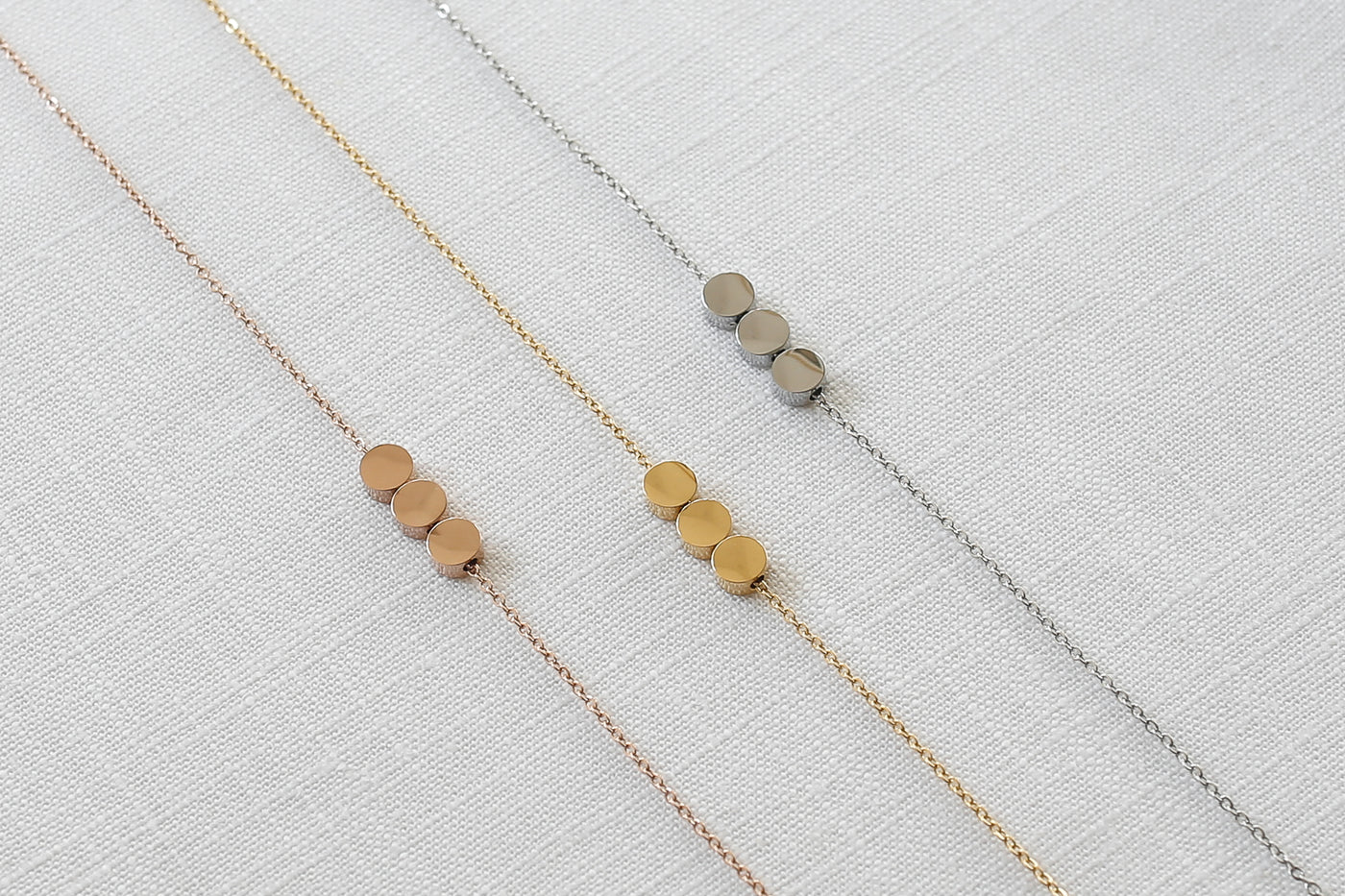 Drei stilvolle Halsketten mit Kreis Anhängern in jeweils Silber, Gold und Rosegold auf Stoff