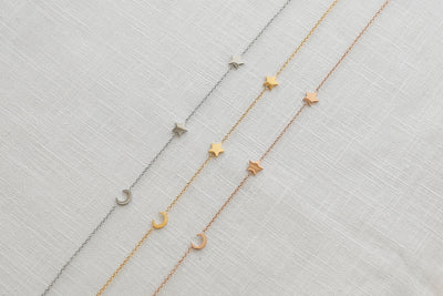 Drei Mond und Stern Anhänger Ketten in Silber, Gold und Rosegold ausgebreitet auf Leinen Stoff.