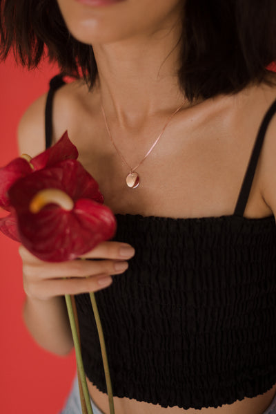 Frau trägt zeitlose Halskette mit Plättchen Anhänger in Rosegoldener Farbe und hält eine Blume auf rotem Hintergrund
