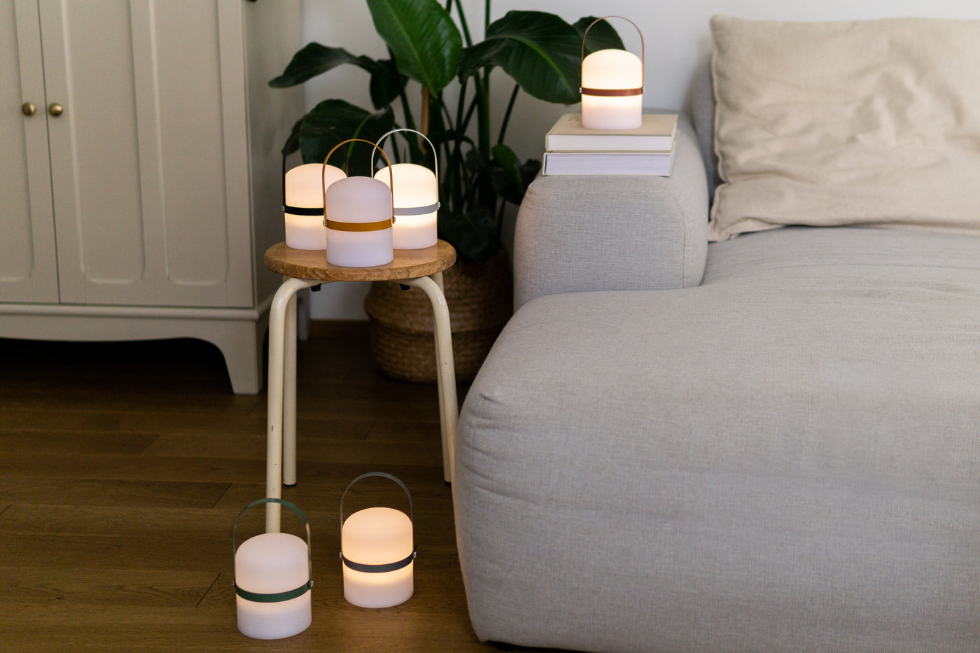 Sechs aufgestellte LED Lampen verteilt auf dem Boden, Holz Hocker und Couch im Wohnzimmer in verschiedenen Farb Variationen