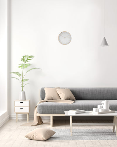 Moderne Wanduhr in weiß hängt über Beistelltisch mit Vase und grauer Couch 