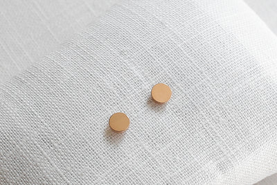 Rosegoldene Ohrringe mit Plättchen Stecker auf Leinen Stoff platziert