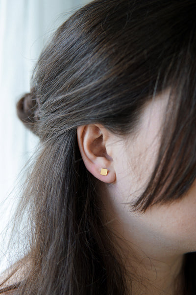 Dame trägt goldene viereckige Ohrringe im Boho Stil 