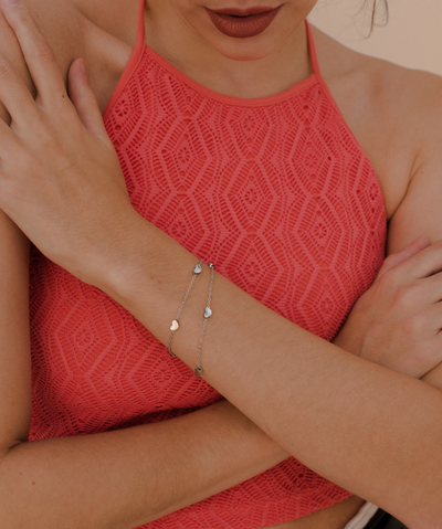 Junge Frau trägt feines silbernes Armband mit kleinen Herz Anhängern im minimalistischen Stil  