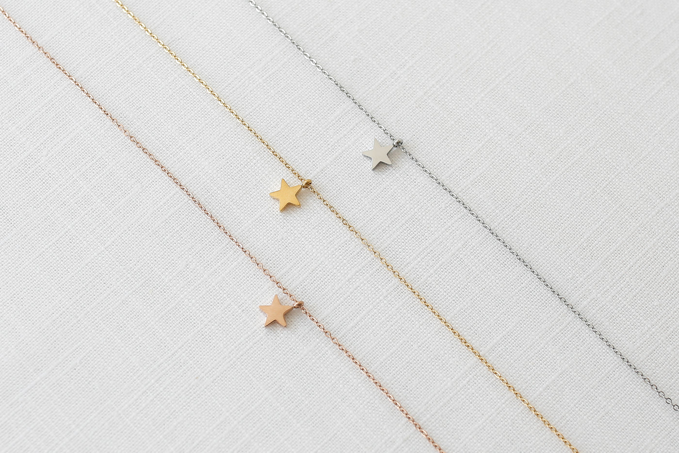 Drei Ketten mit Stern Anhänger in Silber, Gold und Rosegold ausgebreitet auf Leinen Stoff