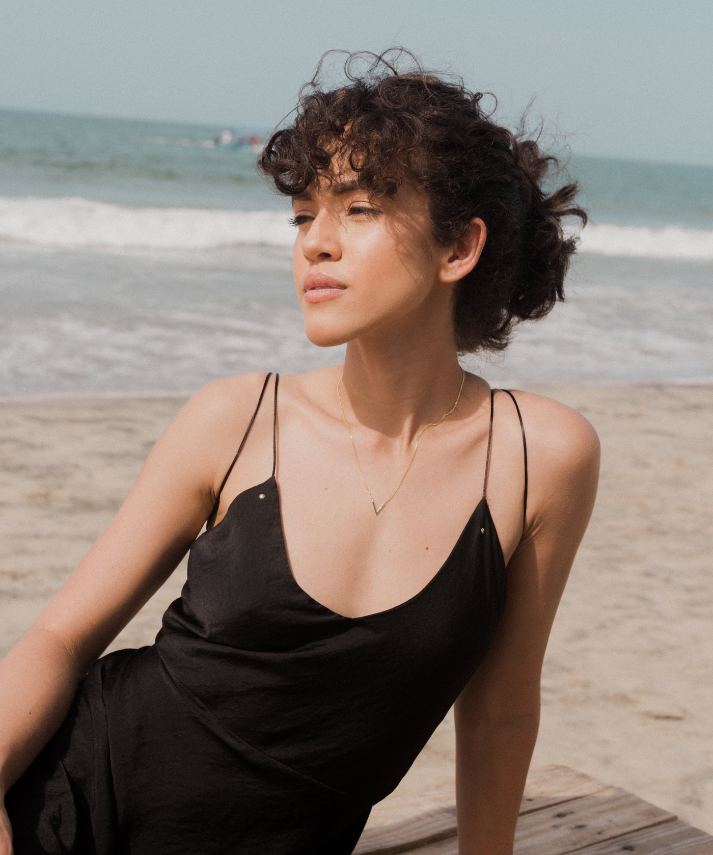 Dame schaut zur Seite und trägt die stilvolle goldene Kette mit V Anhänger am Strand 