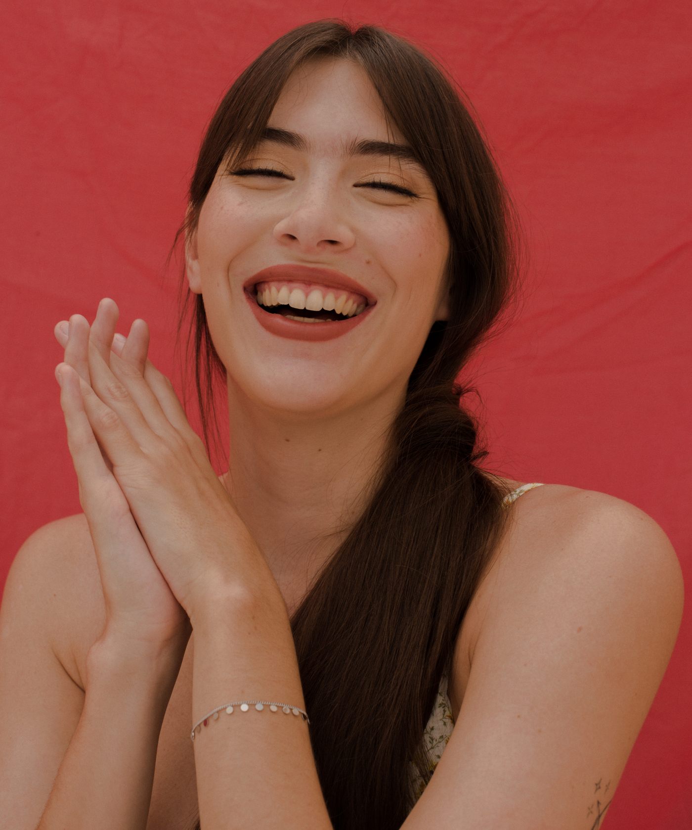 Lachendes Mädchen trägt feines Silber Armband mit Coin Anhängern auf rotem Hintergrund
